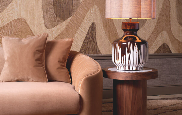 When Materials Converse: Velvet, Marble & Brass- Brown armchair with decorative pillows and a lamp on a wooden side table against a patterned wall.