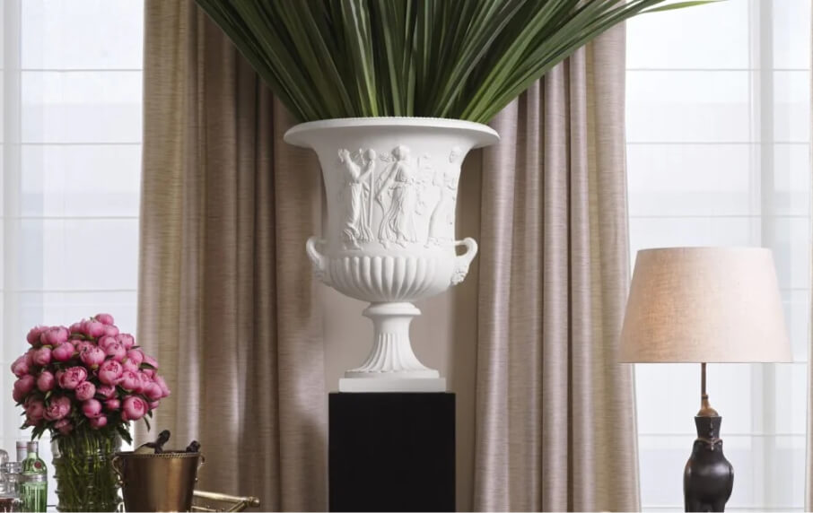 Decorative white urn with green plant against a neutral curtain background